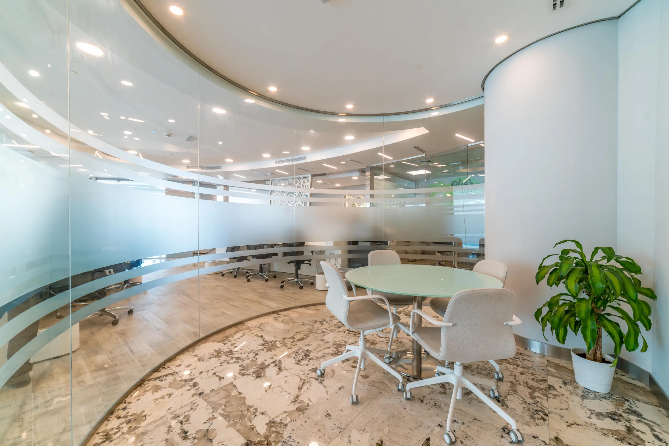 Finished executive office interior with curved glass partitions and integrated lighting.